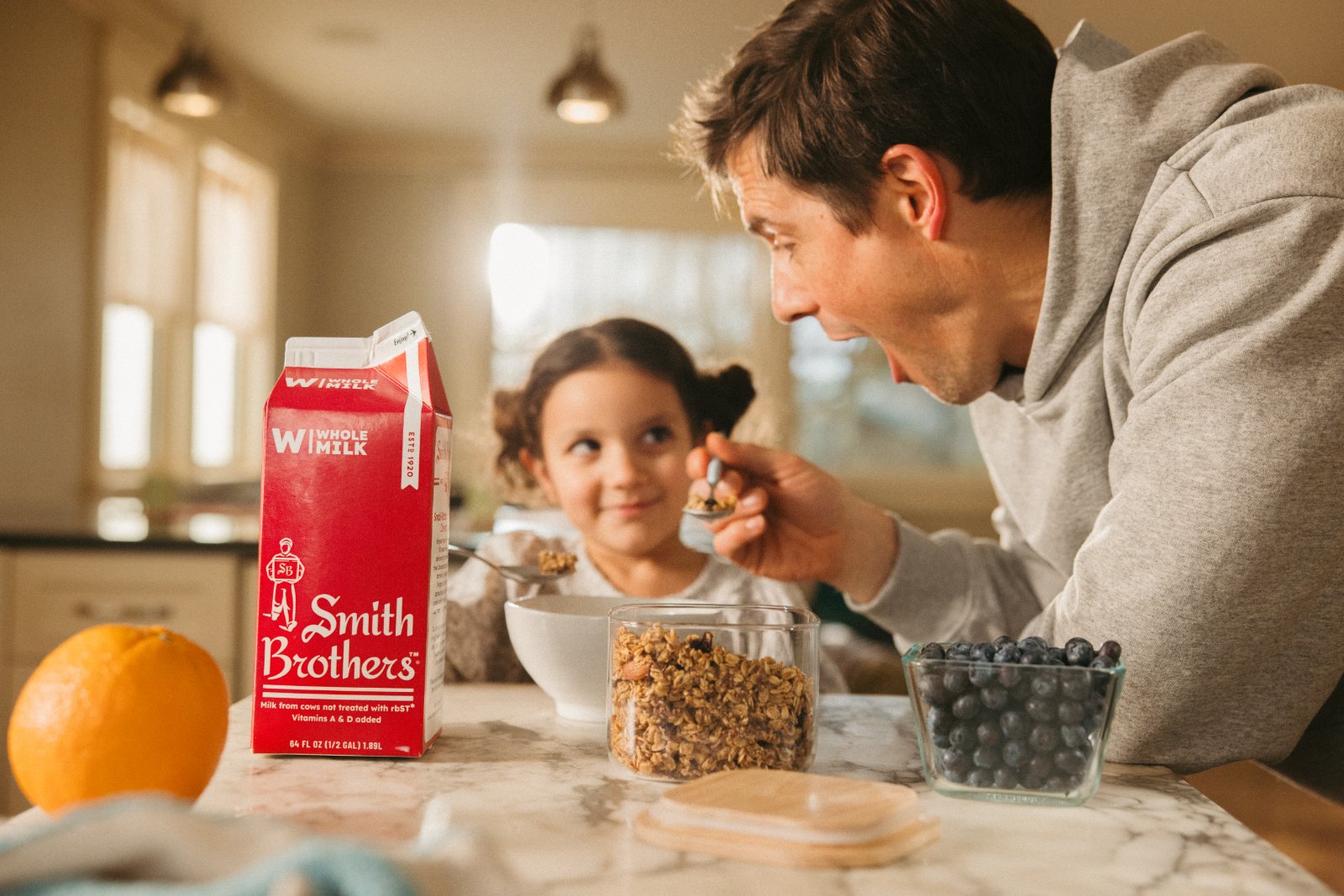 Dad feeding daughter breakfast with Smith Brothers milk on the counter